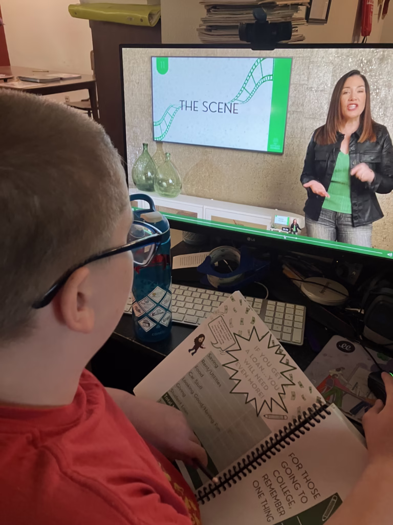 Personal finance is an important life skill to teach in your homeschool. Beyond Personal Finance offers kids real practice in this skill. A teen watches a lesson from Beyond Personal Finance with the student workbook open in front of him.